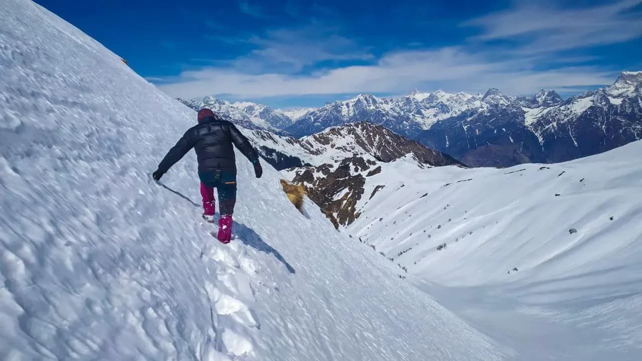 A trekker descending a snow ridge on the Kuari Pass trek, with the Garhwal Himalaya behind